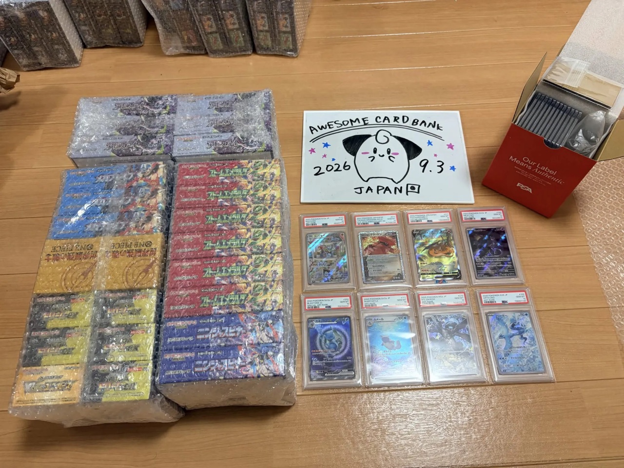 A real order laid out before packing: factory shrink-wrapped boxes in bubble wrap, PSA slabs in sleeves, dated the day it ships.